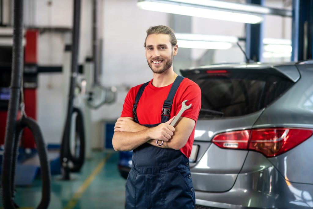 A mechanic smiling and holding a wrench in an auto repair shop.